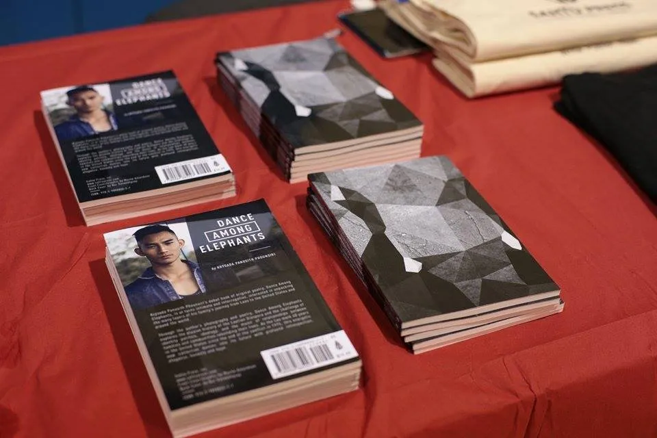 Copies of Dance Among Elephants by Krysada Panusith Phounsiri stacked on a red table, showing the author photo back cover and gray geometric front cover
