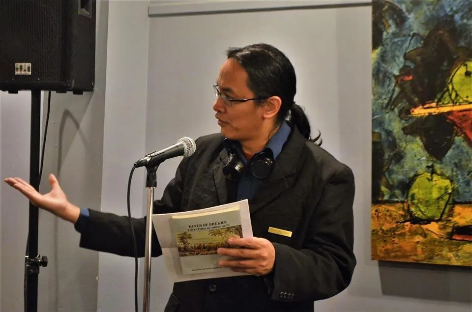 Bryan Thao Worra reading from River of Dreams at a microphone beside an abstract painting